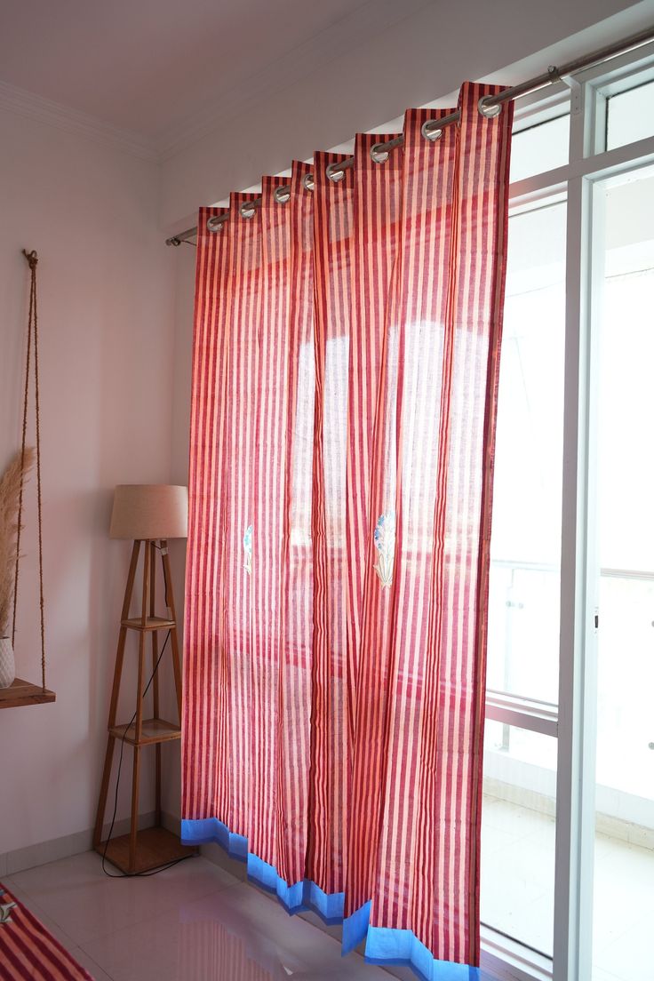 a red curtain hanging in front of a window next to a floor lamp and wooden stand