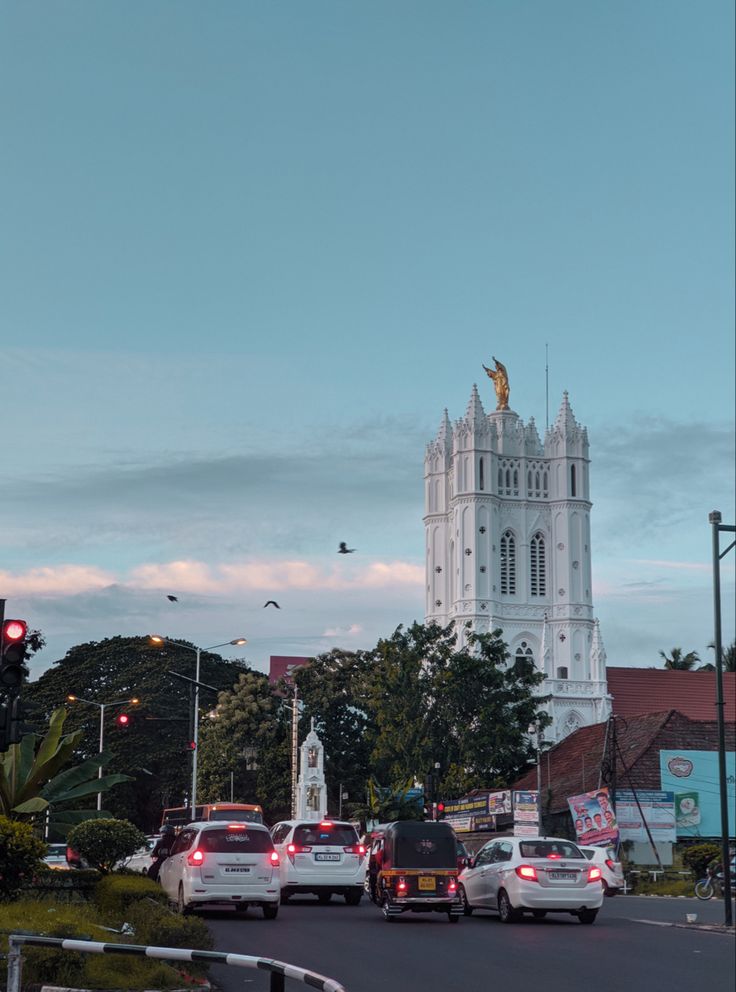 cars are driving down the street in front of a tall building with a steeple