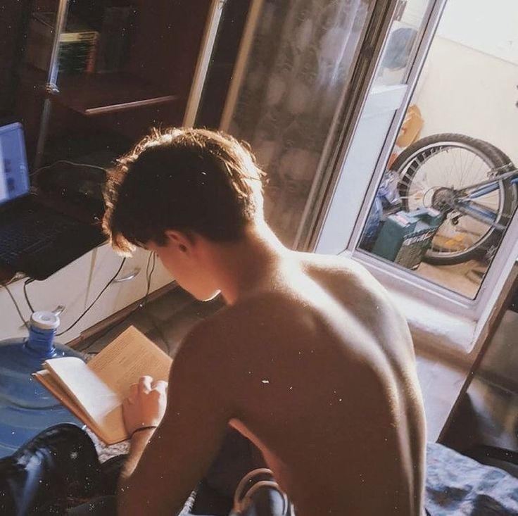 a shirtless young man writing in front of a laptop computer on a desk next to a bicycle