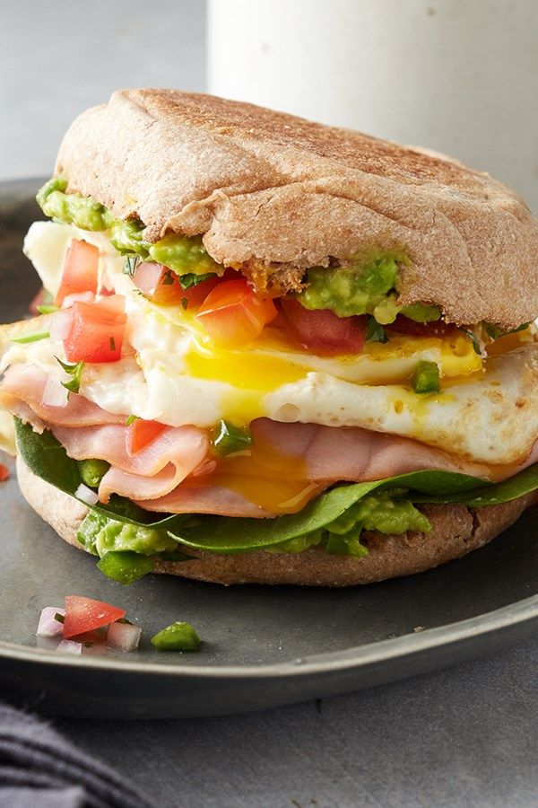 an egg, bacon and avocado sandwich on a plate next to a glass of milk