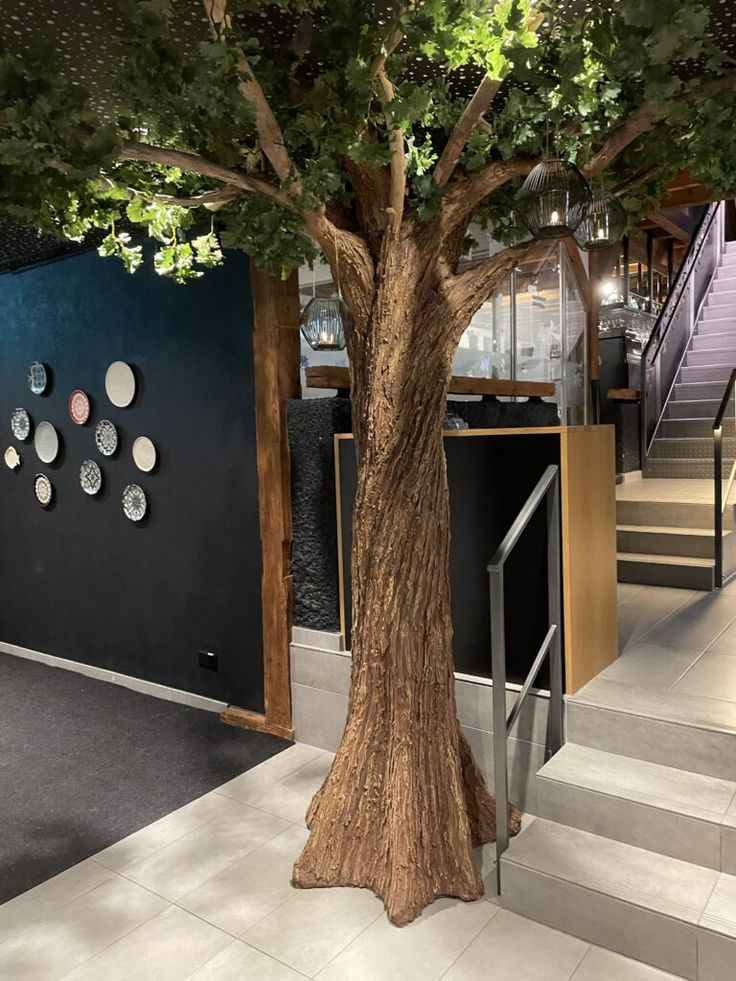 a tree in the middle of a lobby with stairs leading up and down to it