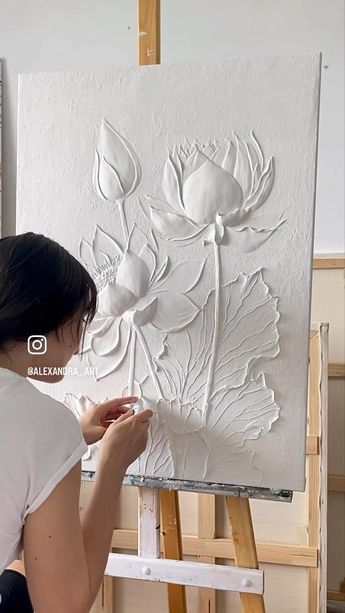 a woman is working on an art work with white paint and flowers in the background