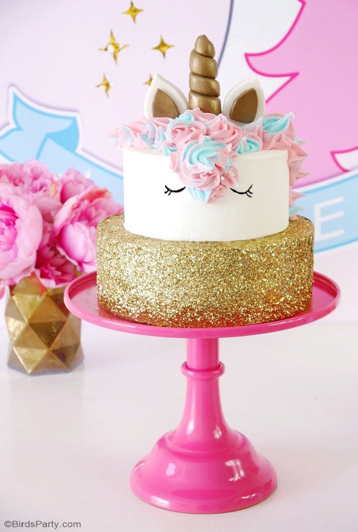 a unicorn cake with pink and gold frosting on a pink plate next to flowers