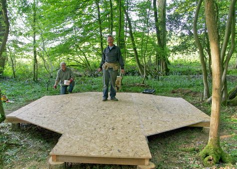 two men standing on top of a wooden platform in the woods