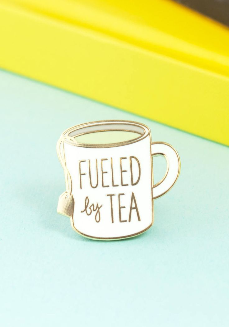 a coffee cup pin with the words fueled by tea on it sitting next to some books