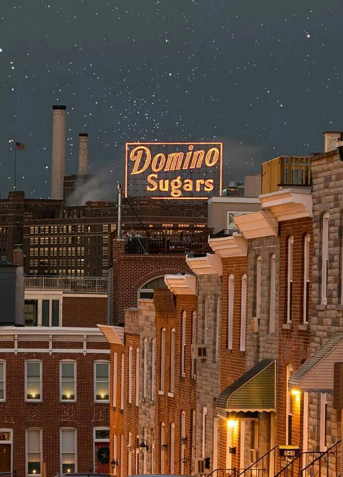 a row of brick buildings with a neon sign above them that reads domino sugars