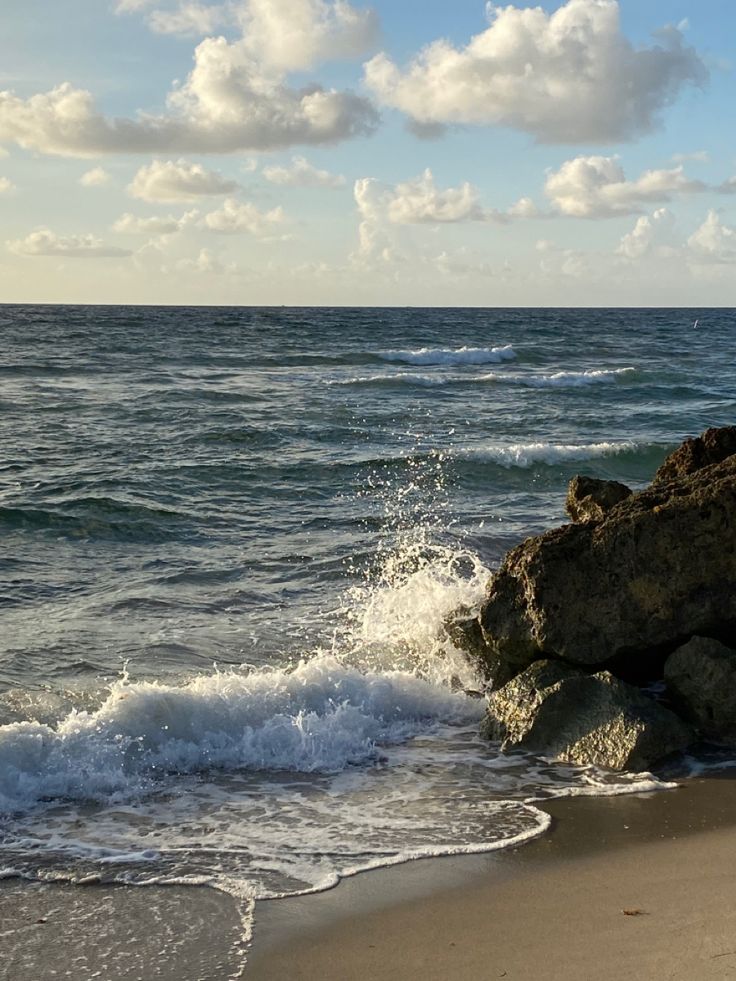 the water is splashing onto the beach with rocks in the foreground and clouds in the background