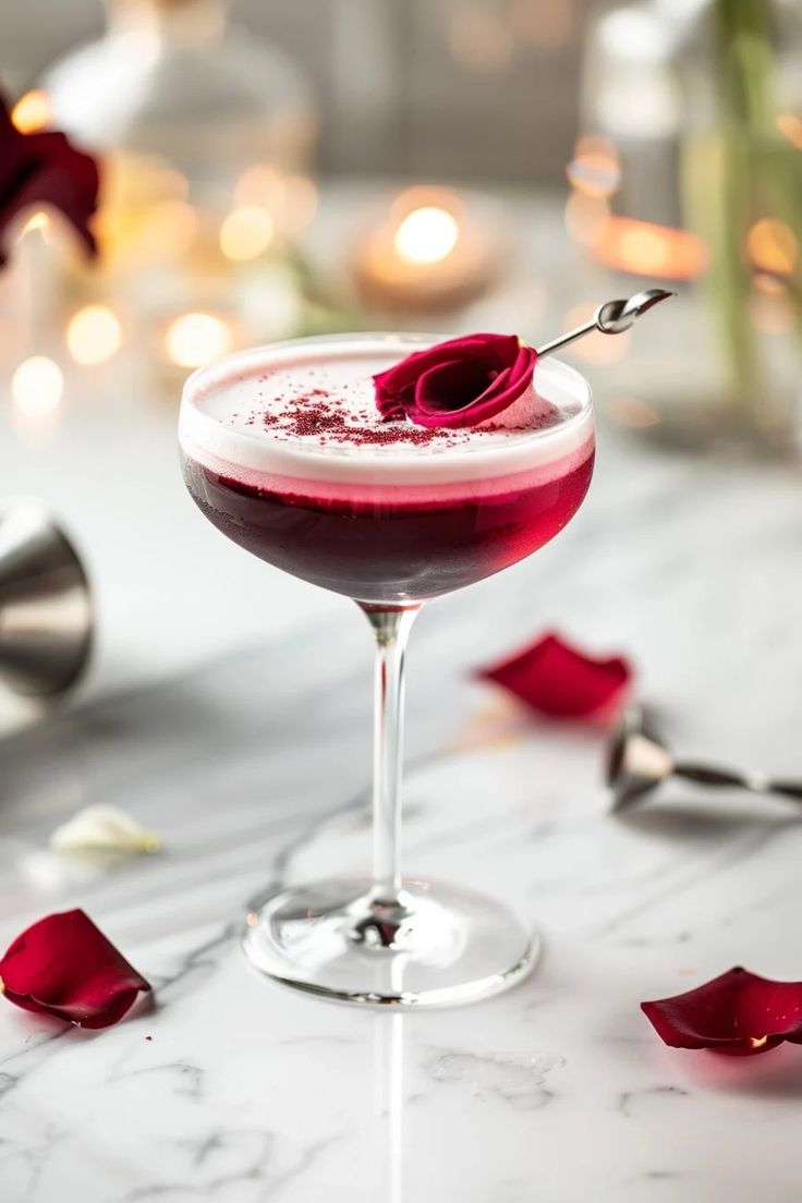 a close up of a wine glass with a drink in it and rose petals on the table