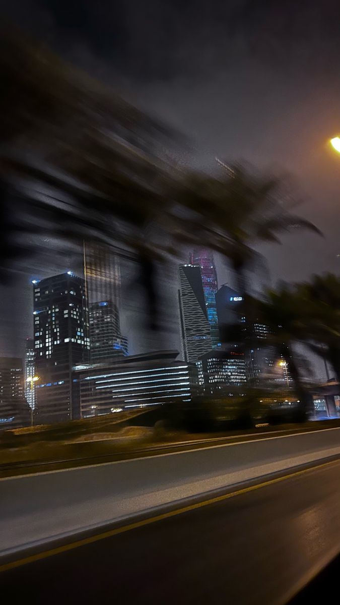 the city skyline is lit up at night with street lights and trees in foreground