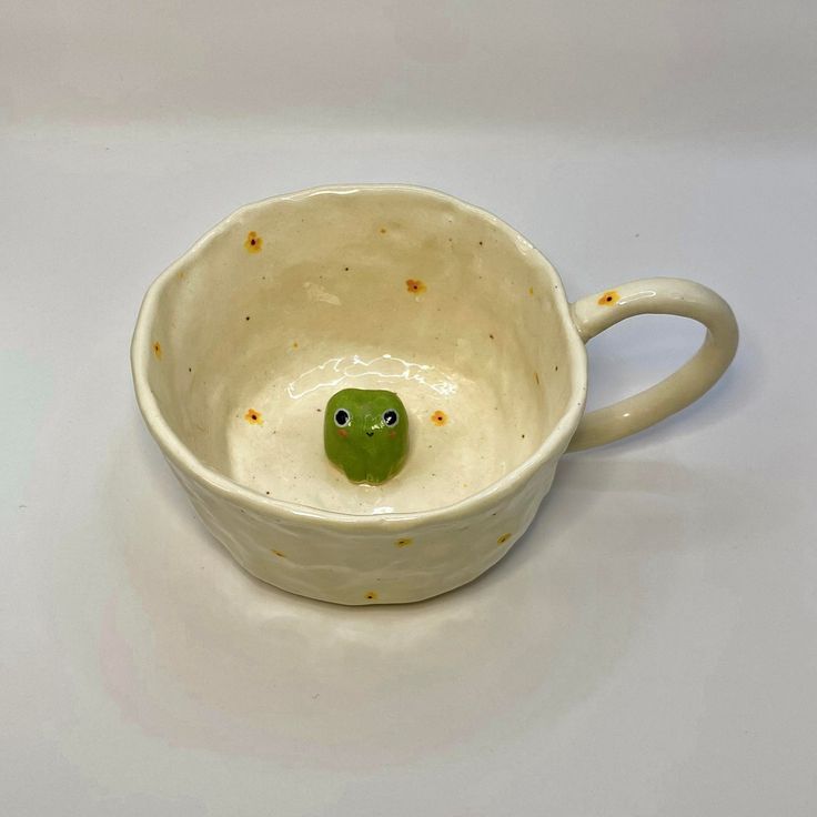 a ceramic cup with a green turtle in it's mouth on a white surface