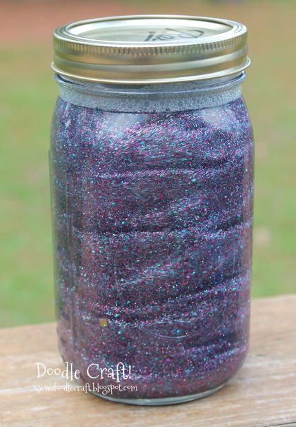 a purple and blue jar sitting on top of a wooden table with grass in the background