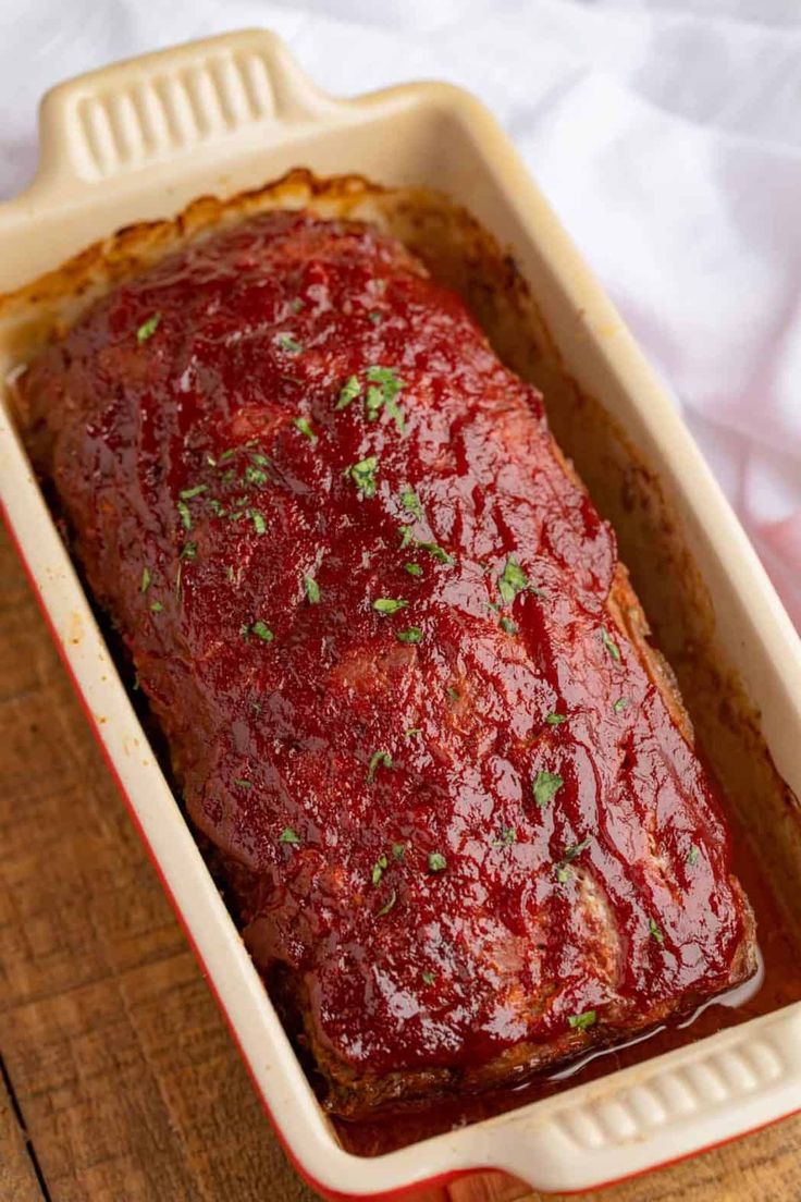 a meatloaf in a red casserole dish on a wooden table