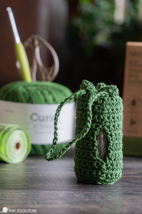 a green crochet bag sitting on top of a table next to yarn and scissors