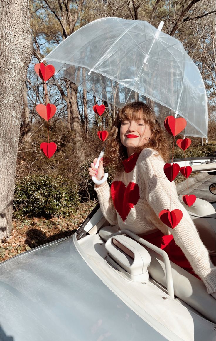 a woman sitting in the back of a car holding an umbrella with hearts attached to it