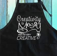 a black apron with the words creativity is messy and i'm very creative on it