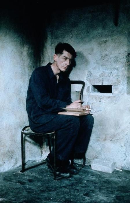 a man sitting in a chair writing on a piece of paper next to a wall