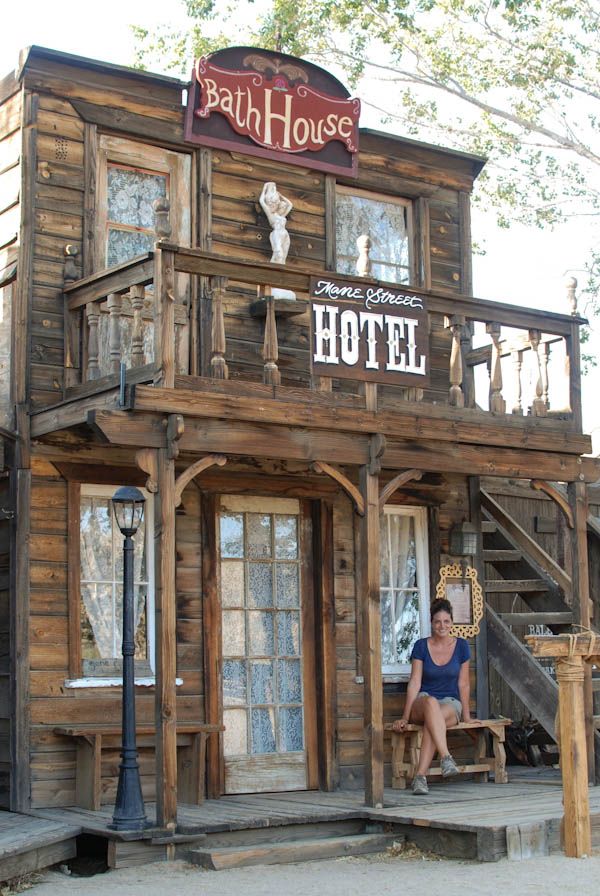 a woman sitting on a chair in front of a wooden building with a sign that reads bath house