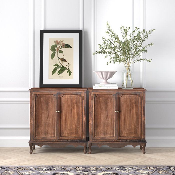 a wooden cabinet sitting next to a vase with flowers in it on top of a rug