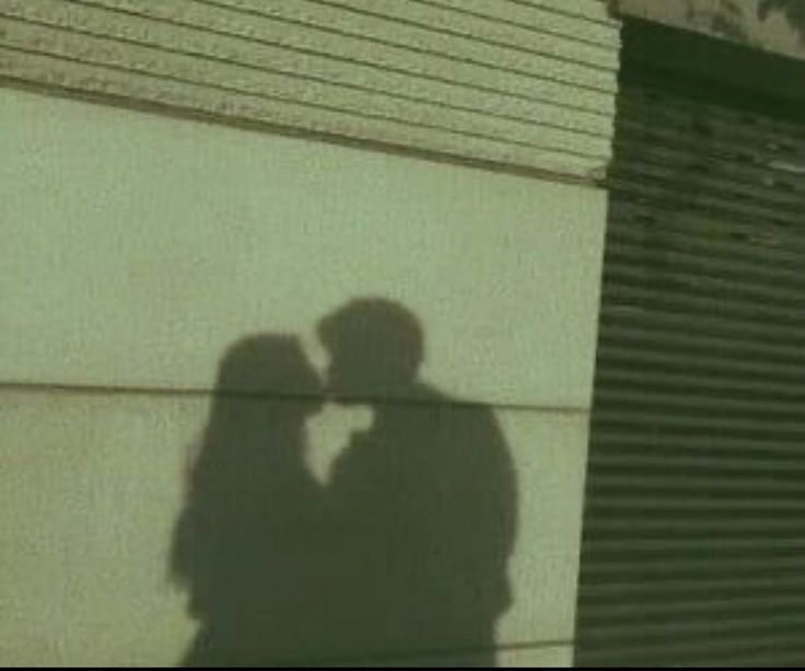 a shadow of two people standing next to each other on the side of a building