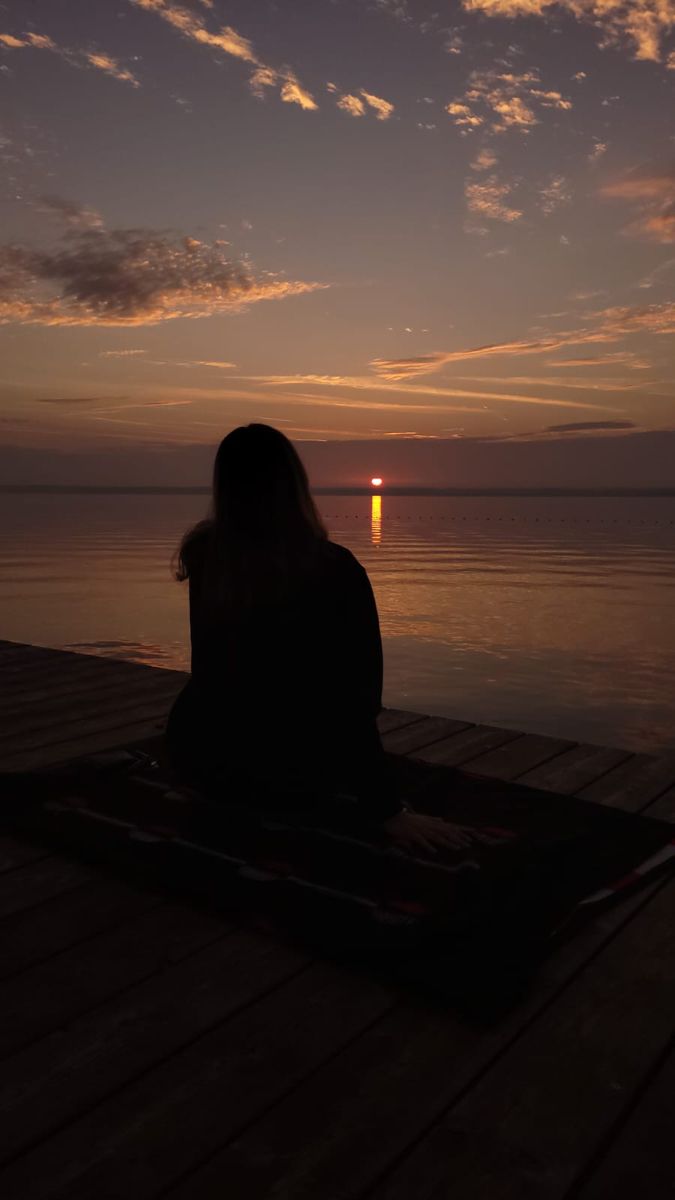 a person sitting on a dock watching the sunset