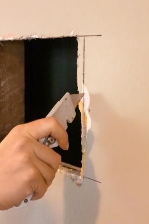 a person holding a remote in their right hand and pointing at the wall that has been torn down