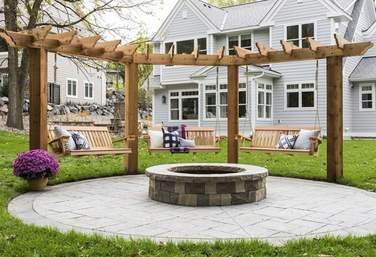 a fire pit in the middle of a yard with benches and flowers on the lawn