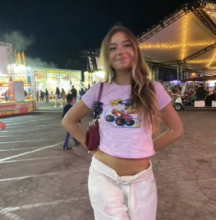 a girl standing in front of a carnival at night with her hands on her hips