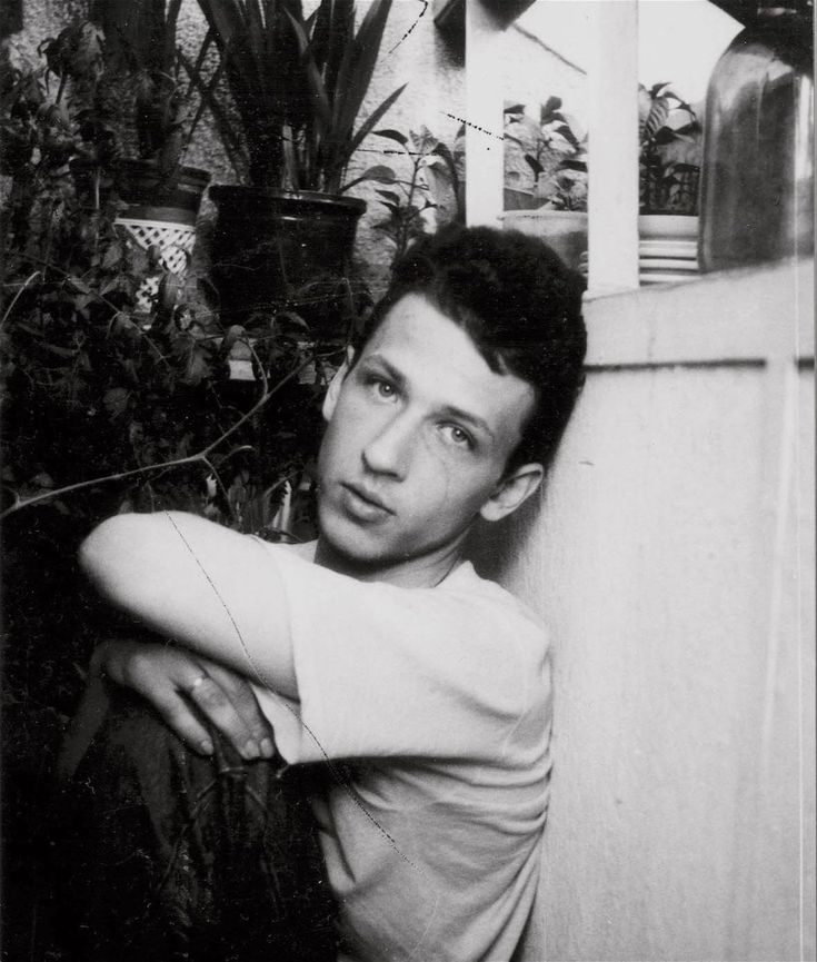 black and white photograph of a man leaning against a wall with plants in the background