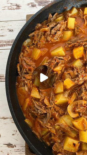 a pot filled with meat and potatoes on top of a wooden table