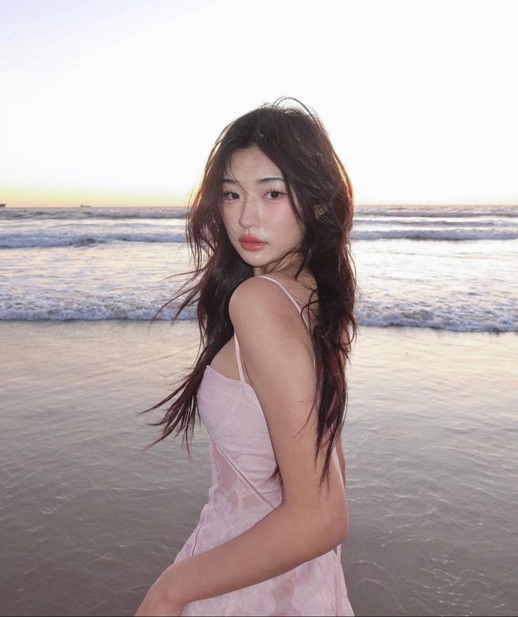 a young woman standing on top of a beach next to the ocean