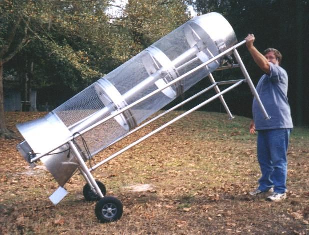 a man standing next to a metal object on top of a grass covered field with trees in the background