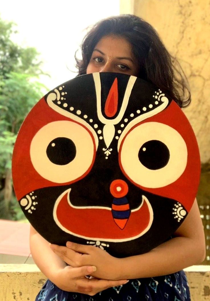 a woman holding up a decorative mask in front of her face