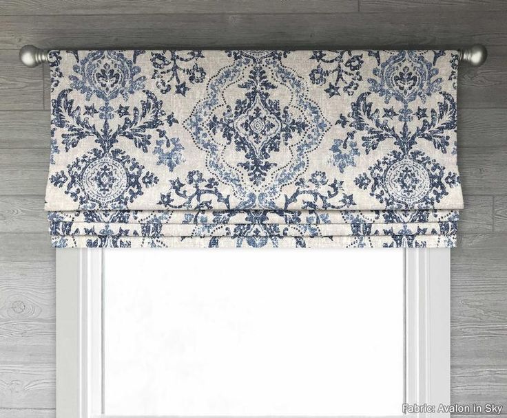 a blue and white roman blind in front of a window with an ornate pattern on it