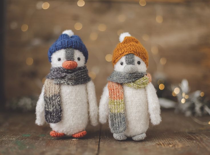 two knitted penguins are standing next to each other on a wooden surface with lights in the background