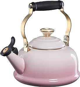 a pink tea kettle with a black handle and gold trimming on the top is shown