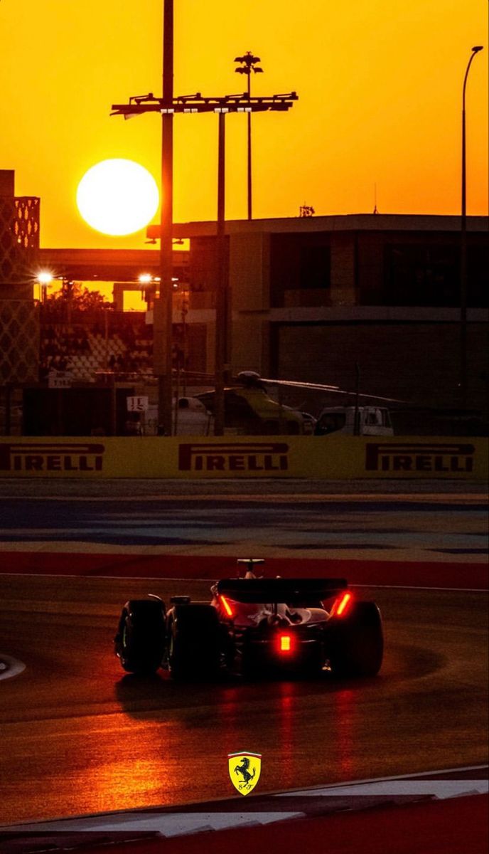 a race car driving on a track at sunset with the sun setting in the background