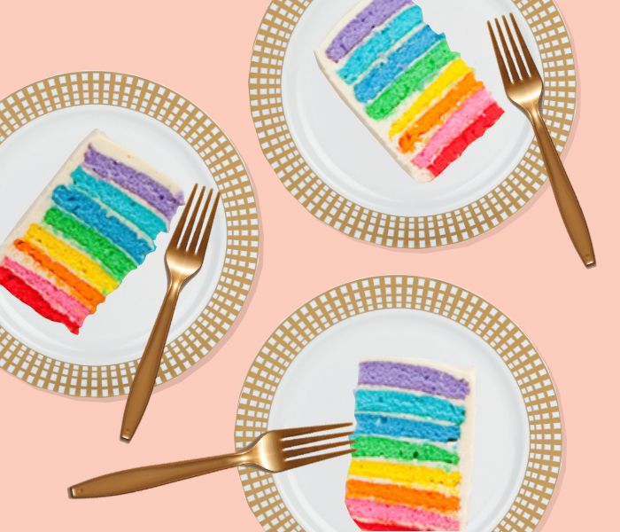 three slices of rainbow cake on plates with gold forks and pink background, top view