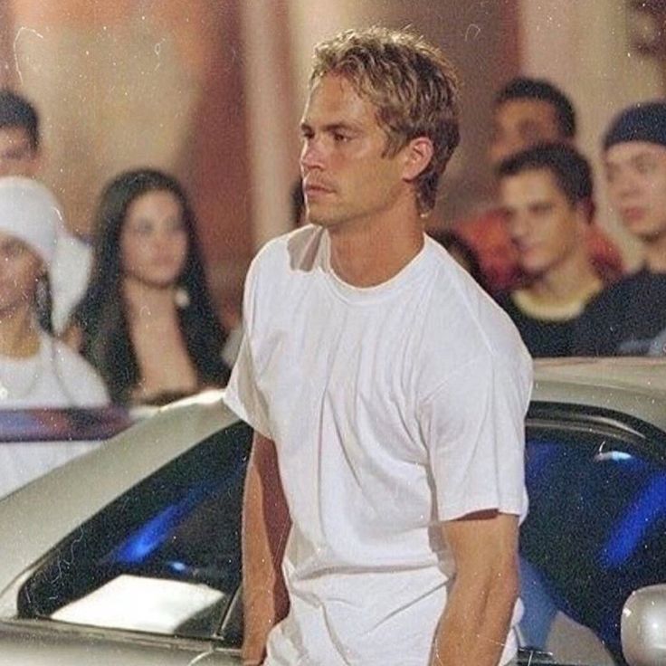 a man standing next to a parked car in front of a group of young people