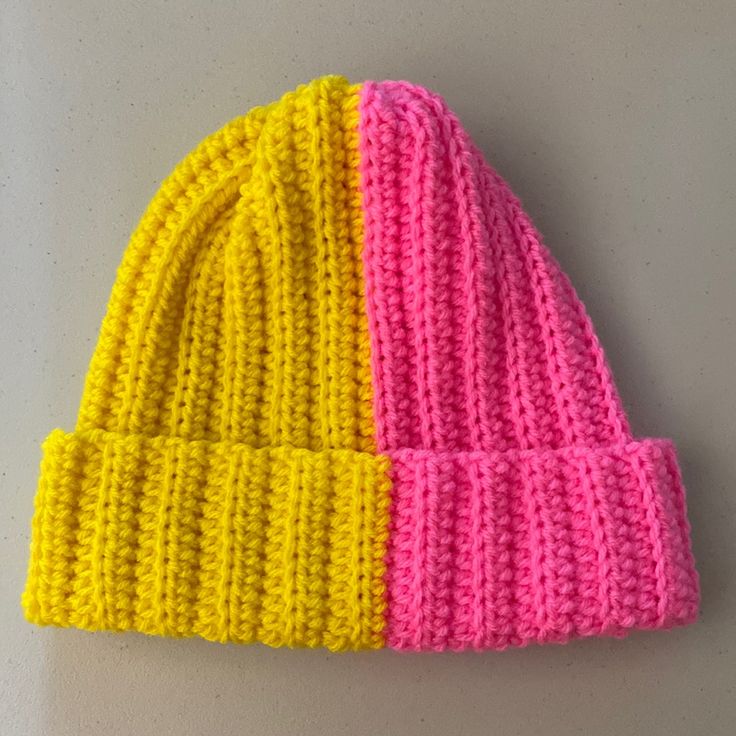 two different colored knitted hats sitting on top of a white table next to each other