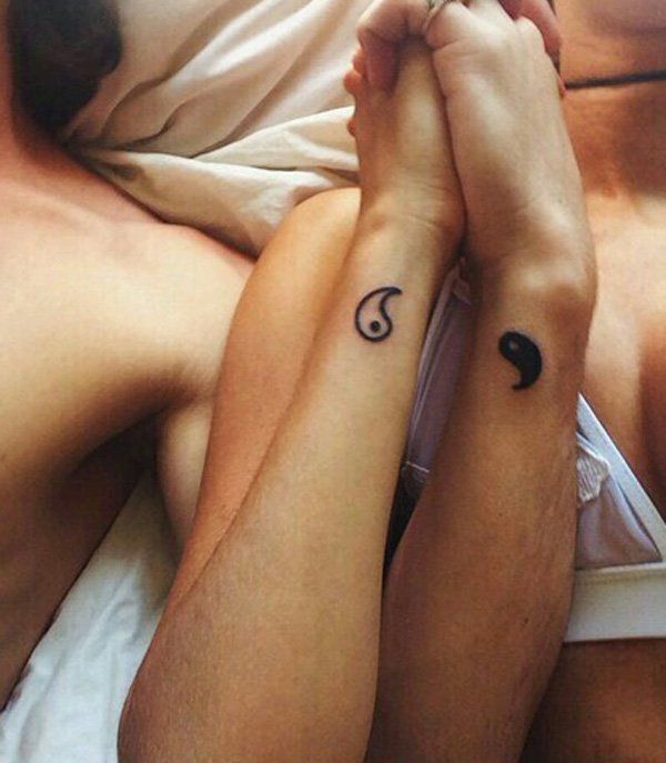 two people laying on top of each other with tattoos on their arms and legs, both holding hands