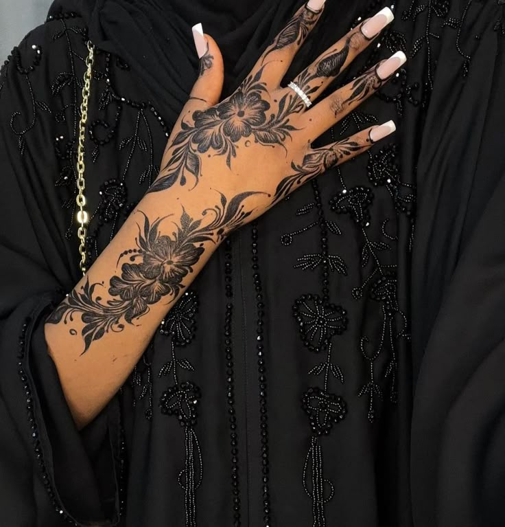 a woman with tattoos on her arm and hand is wearing a black dress while holding onto a gold chain