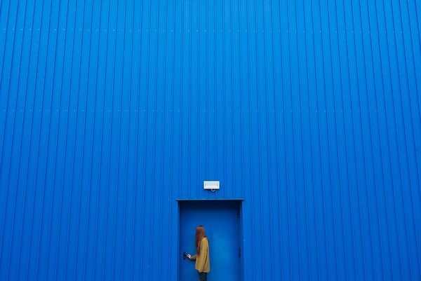 a person standing in a blue door with their hand on his hip and looking at the ground