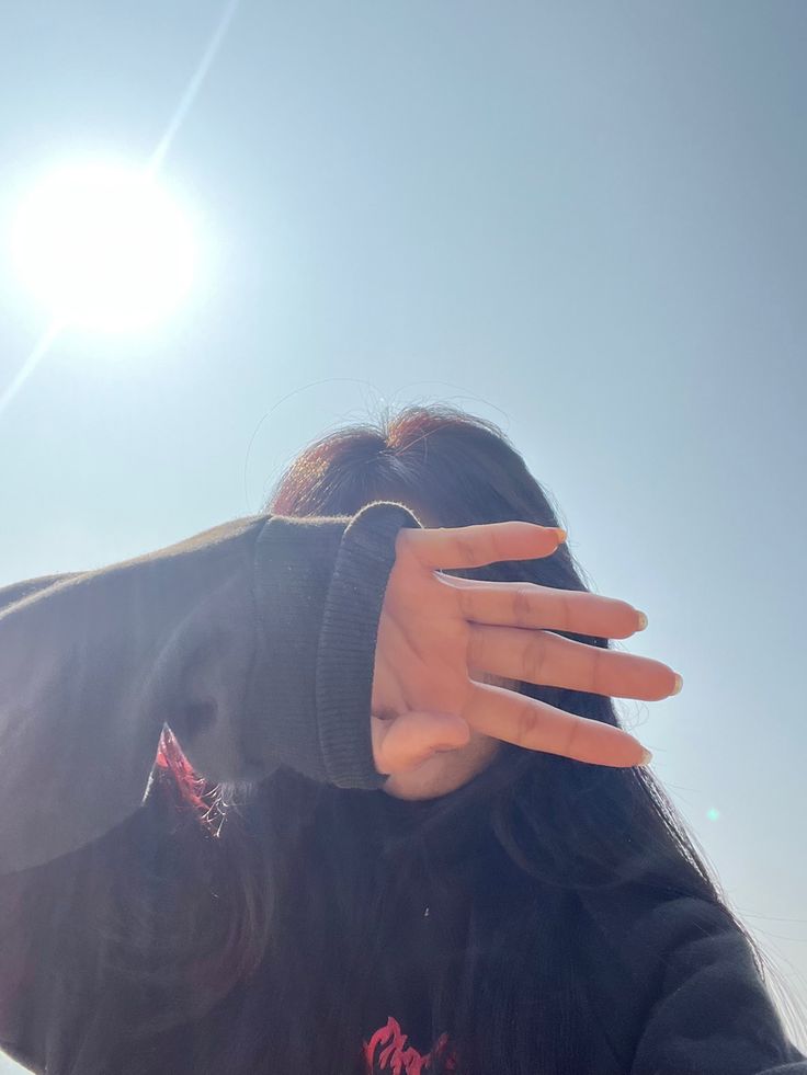 a woman holding her hand up to her face with the sun in the sky behind her