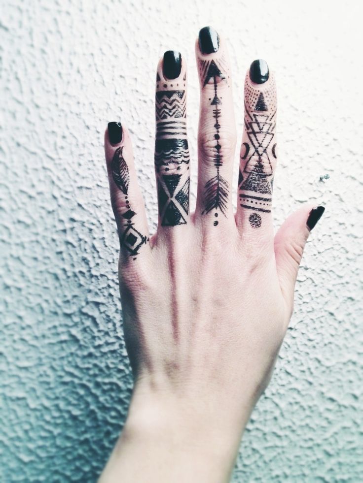 a woman's hand with black and white tattoos on her fingers, holding onto the wall