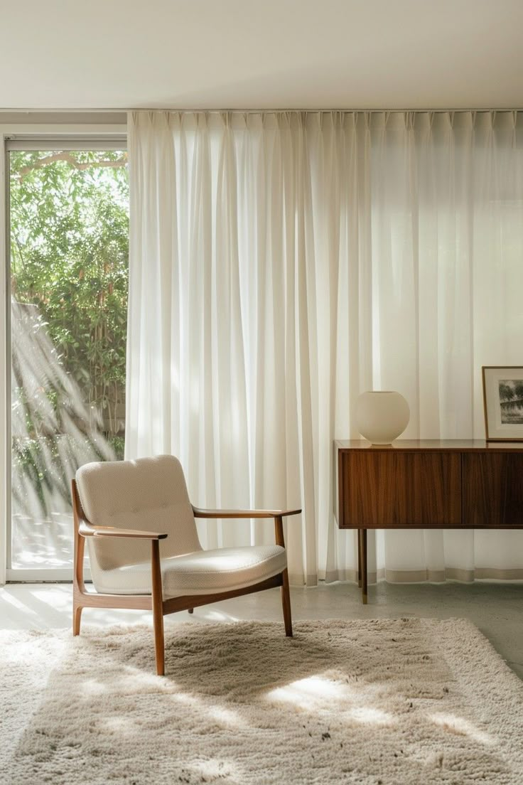 a white chair sitting in front of a window next to a wooden desk and dresser