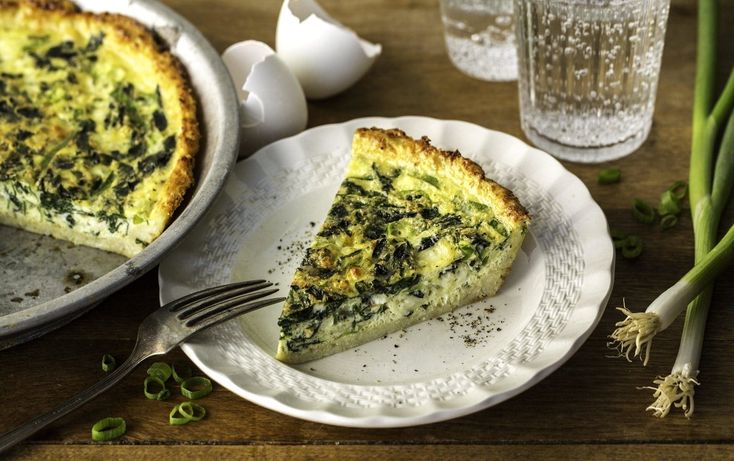 a slice of quiche on a white plate next to an egg and some green onions