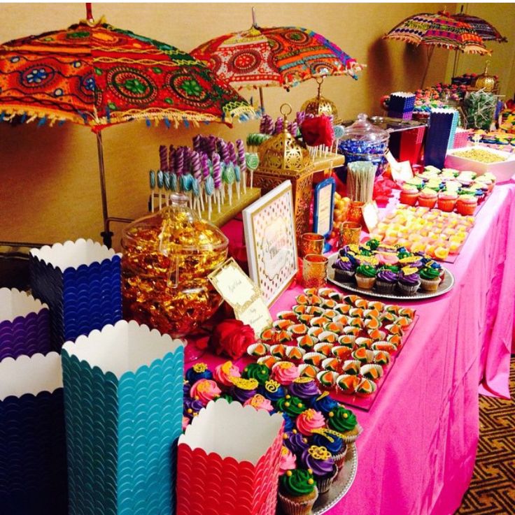 an assortment of colorful cupcakes and treats on a table with umbrellas in the background