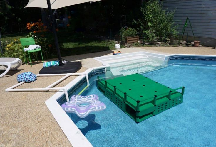 an in ground swimming pool with a green box on the bottom and some chairs around it