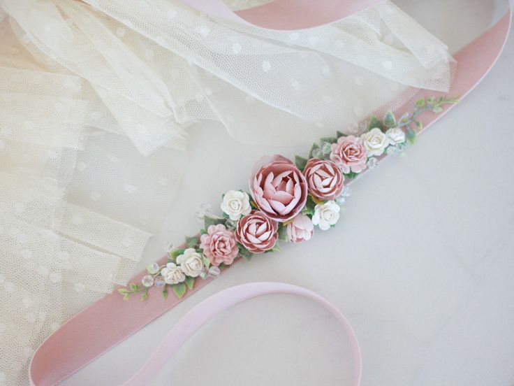 a pink ribbon with flowers on it sitting next to a white lace and tulle