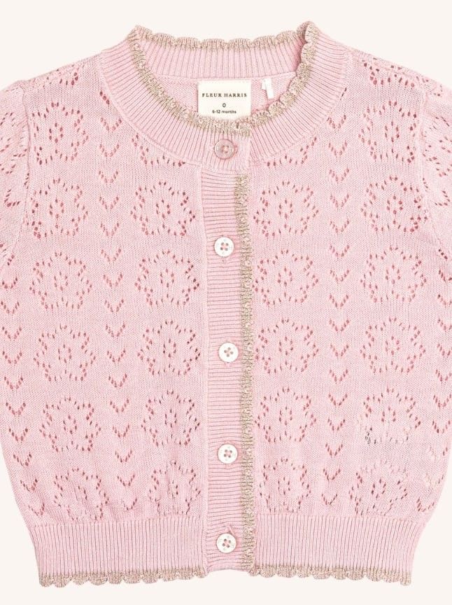 a pink knitted sweater with buttons on the collar and sleeves, in front of a white